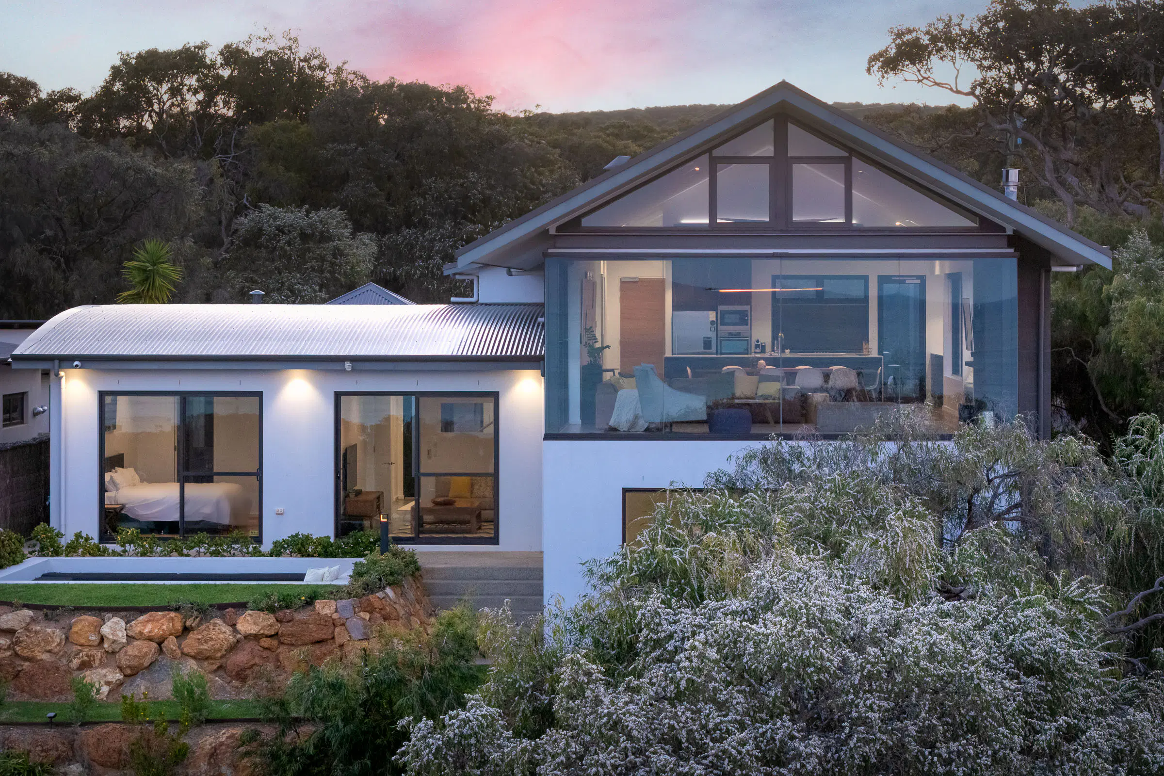 A house at Eagle Bay at dusk — the gable-end glass wall lit from within