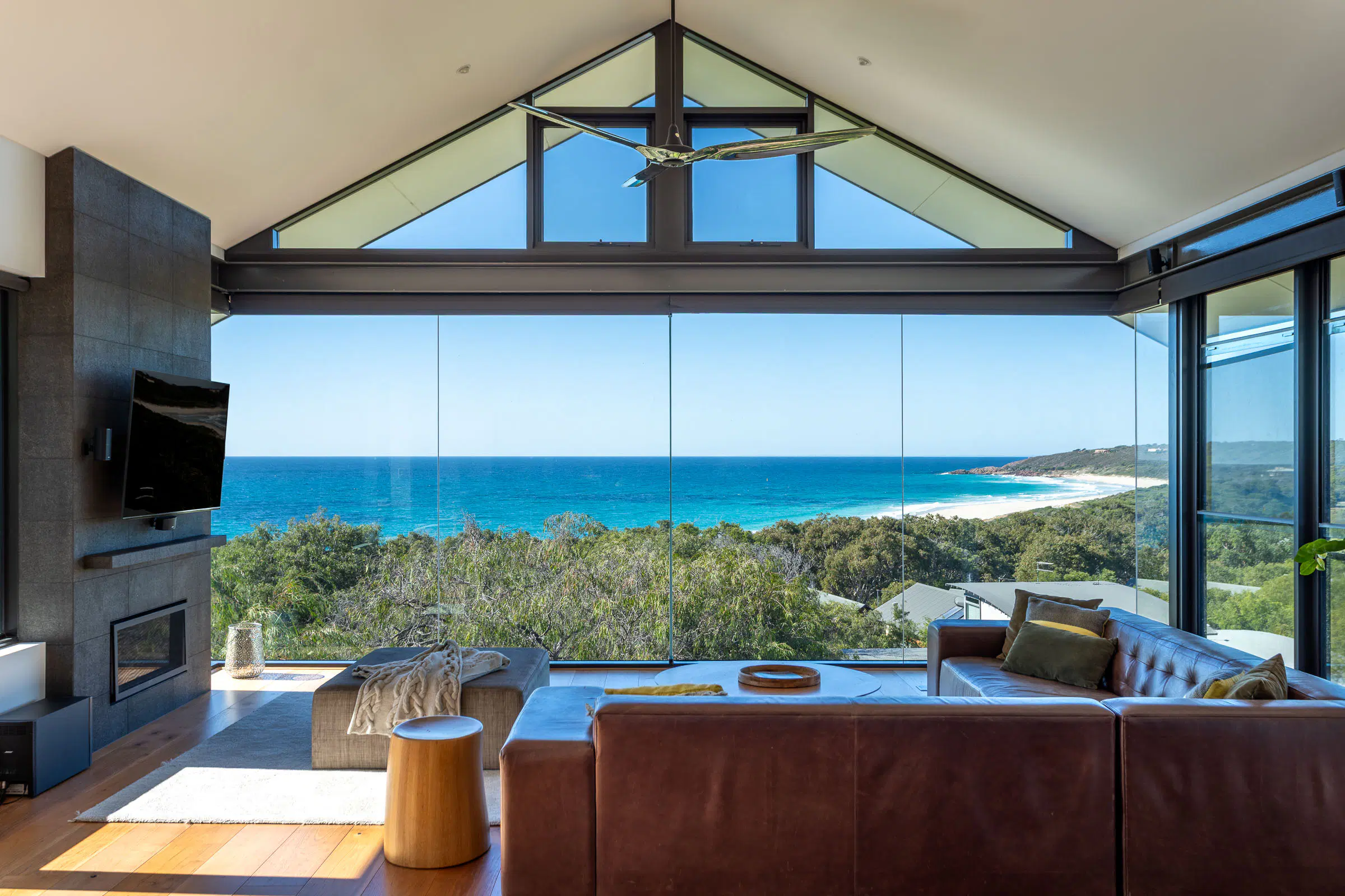 The living room under the gable, glass wall framing the beach